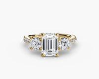 Gold ring with a central emerald-cut diamond and two side stones on a white background